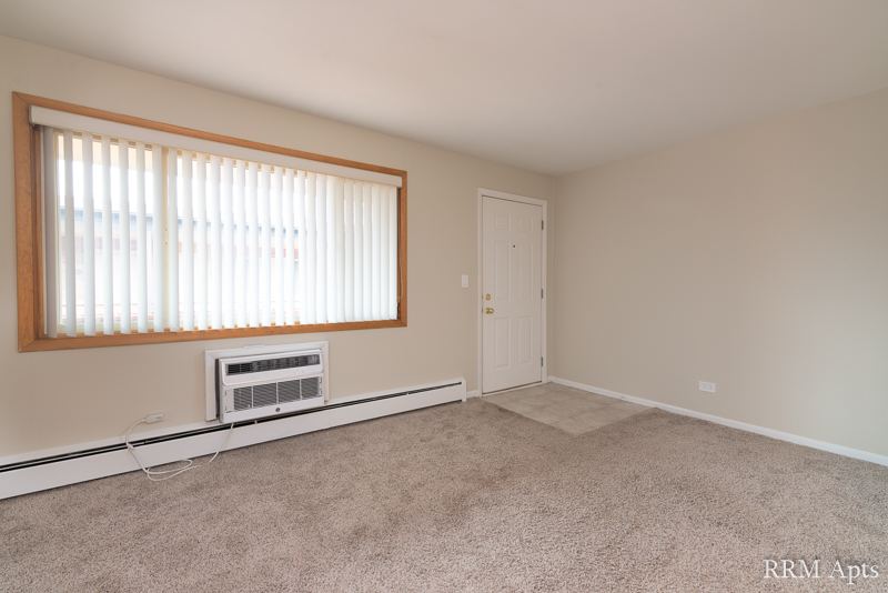 Carpeted living room with wide window, wall air conditioner and front door, Park Avenue apartment 204
